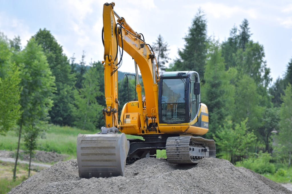 A yellow excavator on a pile of gravel in a lush, green forest setting in Poland.